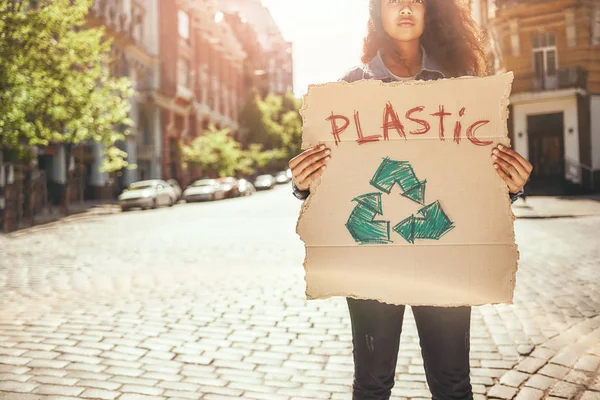 Say no to plastic. Young female activist holding a signboard with word plastic while standing on the road. Ecology concept