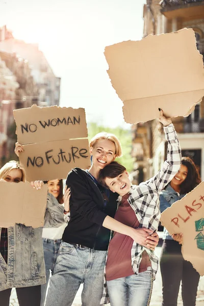 The future is female. Two happy young women are holding signboards and smiling while standing on the road around female activists.