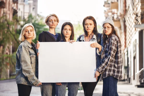 Women power. Group of young female activists are holding blank signboard while standing on the road during a womens march.