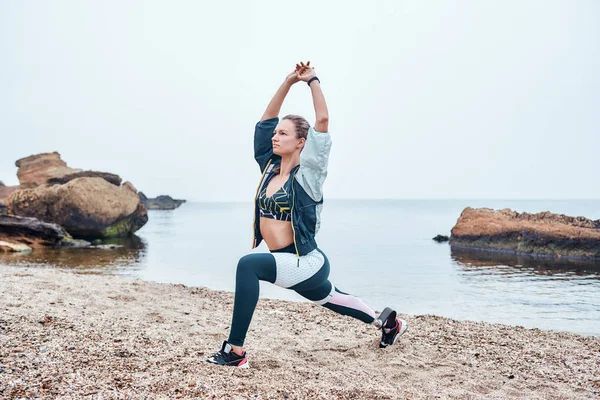Sea Inspiration. Amazing disabled athlete woman in sportswear with prosthetic leg standing in yoga pose at the beach.