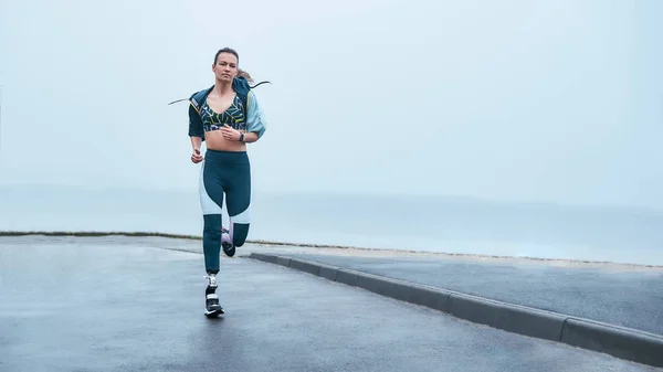 You are stronger than you think. Amazing strong disabled woman in sportswear is running outdoors near the sea