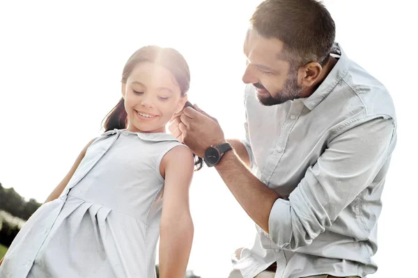 The best father ever. Kind young father adjusting hair clips for his cute daughter while spending time together outdoors