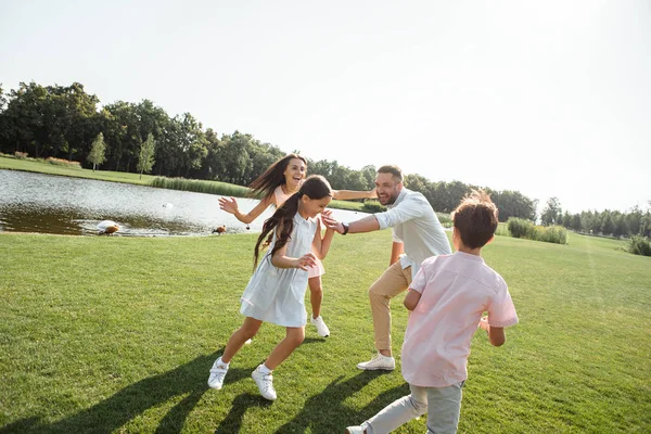 Try to catch me Happy young family playing and smiling while spending free time with family outdoors in park