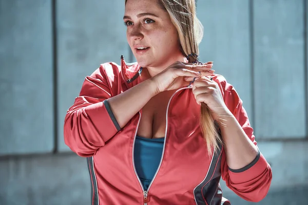 Ready to do my best. Cute plus size woman in sport clothes adjusting her long hair and looking away while standing outdoors