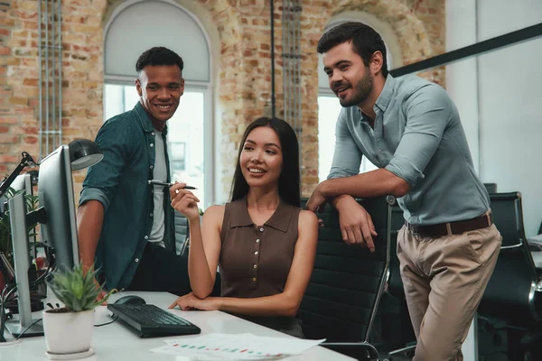 Positive atmosphere. Young beautiful woman pointing at computer monitor and discussing new project with her coworkers while sitting in modern office