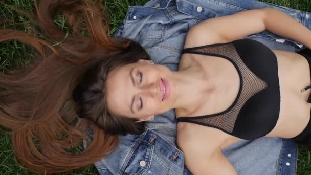 一个美丽的年轻女子的特写在公园的牛仔裤夹克躺在一条长头发 — 图库视频影像