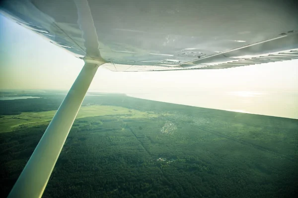 A beautiful aero landscape looking out of a small plane window under the wing. Riga, Latvia, Europe in summer. Authentic flying experience in a sunny, hazy day. Landscape from air.