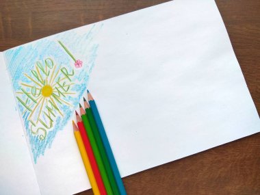 Merhaba yaz albüm resmi ve ahşap bir masa üzerinde renkli kalemler.