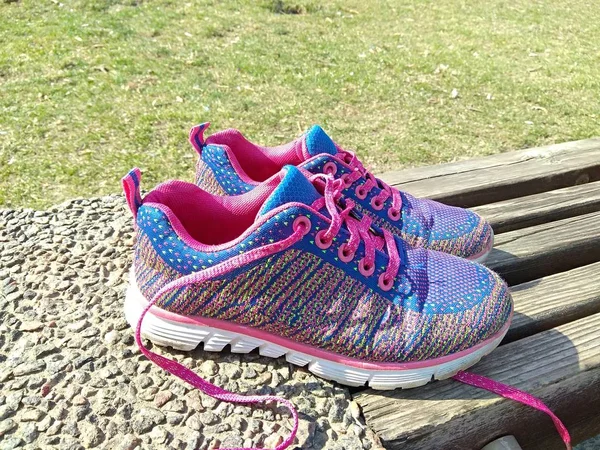 Pink-purple women\'s sneakers on a wooden bench in the park. Spring park, green grass background.