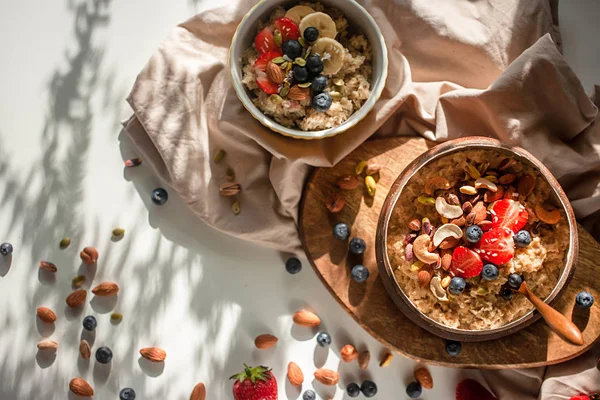 Oatmeal porridge in coconut bowl with wooden spoon on natural wooden tray. Porridge oats with strawberry, pistachios, blueberry, almond and banana. Shadow of sunrise morning. Top view or flat lay