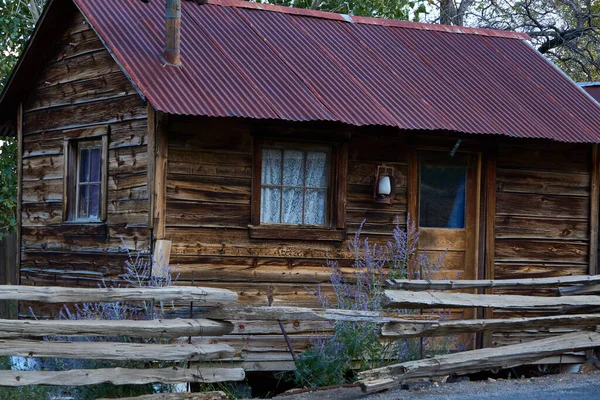 Old rustic cabin with curains in the widows surrounded by split rail fence