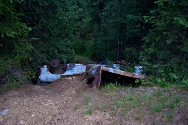 Eski paslı araba şasisi dik bir dağ yolunda baş aşağı duruyor.