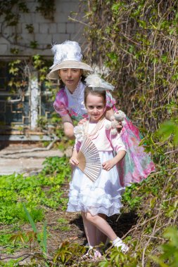 Bayanlar vintage giysiler bir dikey yeşil duvara yakın poz. Beyaz, pembe, yeşil renkli bir elbise, şapka, bir fan, boncuklar imitasyon takı ve bir oyuncak ayı. Anne ve kızı bir yaz parkta.
