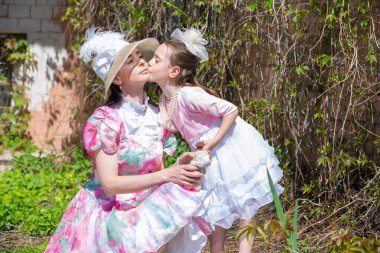 Çok neşeli ve sevimli bir kız öpücük anne vintage şapkalı bir yanak ve bahar bahçe beyaz pembe yeşil elbise. Anne ve kızı bir yaz parkta.