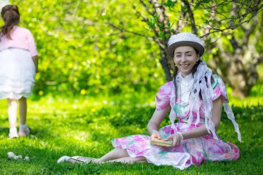 Küçük bir kız güzel beyaz klasik aristokrat elbiseler yeşil alanda parlak güneşli bir parkta kulağında annesi ile sırlarını paylaşmak için acele. Bir yaz parkında anne ve kızı.