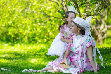 Küçük bir kız güzel beyaz klasik aristokrat elbiseler yeşil alanda parlak güneşli bir parkta kulağında annesi ile sırlarını paylaşmak için acele. Bir yaz parkında anne ve kızı.