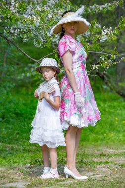 Anne ve kızı bahar ormanda çiçek açması bir elma ağacı arka planı poz. Onlar ışık tarihsel elbiseler, şapka ve ellerinde bir fan ile stand. Aile bir yaz parkta.