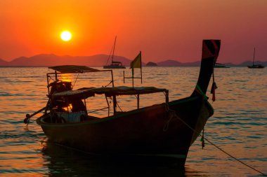 Parlak renkli turuncu güneşin rengi gün batımında sahilinde longtail balıkçı teknede silüeti. Tropikal ufuk Adaları ve Katamaran ile. Railay Beach günbatımında. Krabi, Tayland.