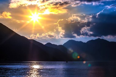 Adriyatik Denizi Körfezi'nin mavi su pitoresk ve çekici dağlarda siluetleri yukarıda bulutların arkasında parlak sarı güneş ışınları. Sunset Bulvarında Boka Kotorska Bay, Kotor, Karadağ.