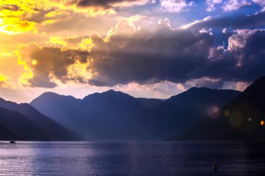 Adriyatik Denizi Körfezi'nin mavi su pitoresk ve çekici dağlarda siluetleri yukarıda bulutların arkasında parlak sarı güneş ışınları. Sunset Bulvarında Boka Kotorska Bay, Kotor, Karadağ.