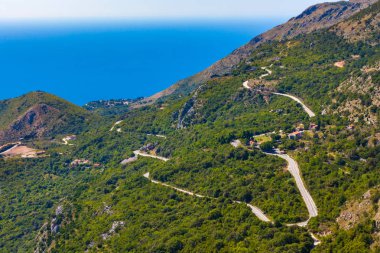 Kıvrıla kıvrıla - Adriyatik Denizi kıyısında lider kayalık yamaçlar arasında yoğun bir yeşil orman içinde bir dağ asfalt yol. Karadağ dağlarda yaz.