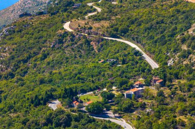 Kıvrıla kıvrıla - Adriyatik Denizi kıyısında lider kayalık yamaçlar arasında yoğun bir yeşil orman içinde bir dağ asfalt yol. Karadağ dağlarda yaz.