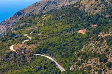 Kıvrıla kıvrıla - Adriyatik Denizi kıyısında lider kayalık yamaçlar arasında yoğun bir yeşil orman içinde bir dağ asfalt yol. Karadağ dağlarda yaz.