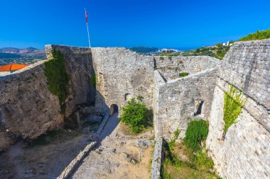 Yüksek taş duvarlar, antik bir binada köşesinde çekilen ulusal bayrak çevrili kalenin avlusunda. Yaz manzara kale kent Bar, Karadağ.