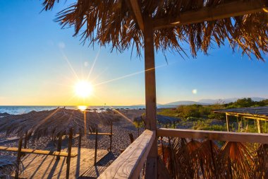 Günbatımı ile renkli güneş ışınları Adriyatik Denizi, yolları şezlong ve şemsiye kıyısında ahşap ve saman kum rekreasyon alanı'nda yapılmış. Kumsalda Ada Bojana, Ulcinj, Karadağ.