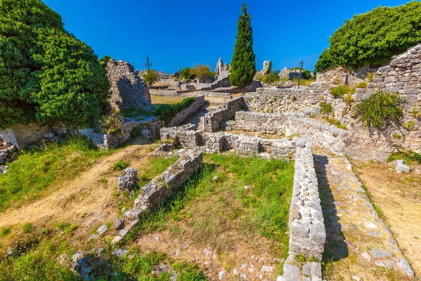 The inner courtyard of the ancient city with dilapidated walls, the land overgrown with green grass with trodden paths, view from above. Summer landscape in Fortress Old Bar Town, Montenegro.