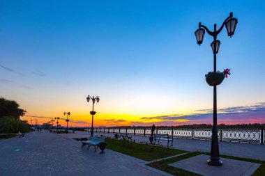 Yaya bir çit karanlık akşam, nehir alacakaranlıkta ve gökyüzü parlak renkler renkli günbatımı, silüeti Volga Nehri kıyısındaki. Petrovskaya dolgu, Astrakhan, Rusya Federasyonu.