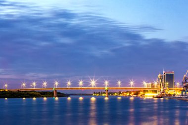 Alacakaranlıkta geceleri sokak yol beton köprü destekler Volga Nehri geçip, aydınlatmak, yeşil orman ve endüstriyel farklı kıyısında rıhtım. Yeni bir köprü, Astrakhan, Rusya Federasyonu.