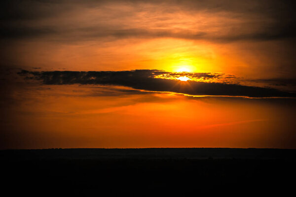 Cloud silhouette on a bright colorful orange sky hiding the yellow sun over the black steppe plain.