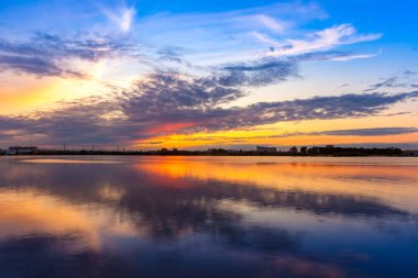 Kazanka Nehri, Kazan, Tataristan, Rusya. Mavi gökyüzünde beyaz bulutlu parlak turuncu gün batımı suya yansıyor. Rus şehrinin kıyısında romantik bir akşam.
