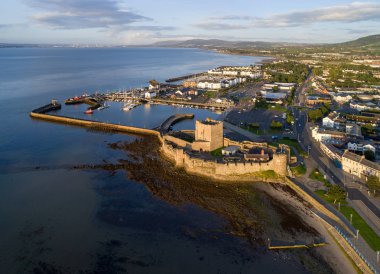 Carrickfergus gündoğumu ışık Belfast yakınındaki Ortaçağ Norman Kalesi. Marina, yatlar, otopark, dalgakıran, groyne, çökeller ve uzak Belfast görünümünde arka plan ile havadan görünümü