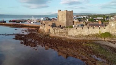 Carrickfergus gündoğumu ışık Belfast yakınındaki Ortaçağ Norman Kalesi. Hava 4 k uçuşu su yansıma, marina, kasık, dalgakıran, kasaba ve uzak Belfast görünümünde arka plan video.