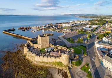 Belfast Lough. Carrickfergus gündoğumu ışık Ortaçağ Norman Kalesi. Marina, yatlar, otopark, dalgakıran, çökeller ve uzak Belfast görünümünde arka plan ile havadan görünümü