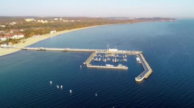 Ahşap iskele, marina, yatlar, küçük yelkenli yelkenli yelken ve kumlu plaj ile Polonya Sopot resort. Gündoğumu ışığında havadan 4k uçuş videosu.