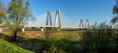 Polonya 'nın Krakow kentindeki Vistula Nehri üzerindeki modern çift kablolu köprü. Gün doğumunda ağaçlarla dolu geniş bir manzara.