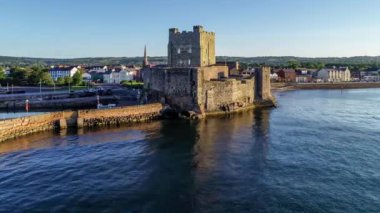 Belfast Lough, Carrickfergus 'taki Ortaçağ Norman Kalesi' nde gün doğumunda Belfast yakınlarında. Marina, dalgakıran, yat, park yeri, kasaba ve arka planda Belfast manzaralı 4K uçuş videosu