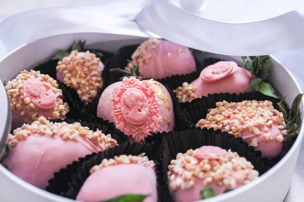 Morangos cobertos com cobertura de chocolate rosa com nozes em uma caixa redonda com uma tampa transparente com uma fita cinza e um arco em mármore cinza — Fotografia de Stock