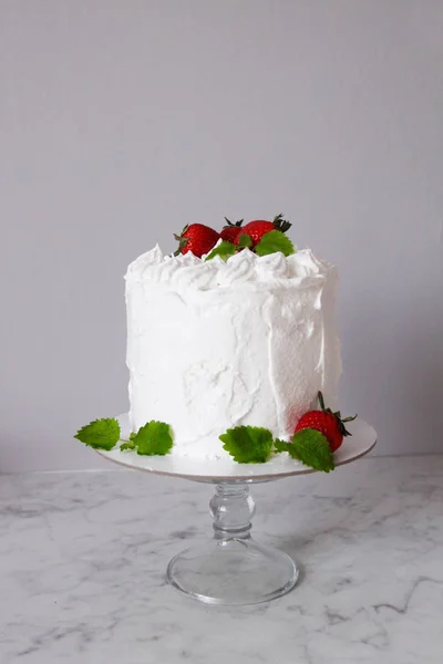 Grande bolo delicioso branco com creme e decorado com morangos e hortelã em um suporte transparente em um fundo cinza — Fotografia de Stock