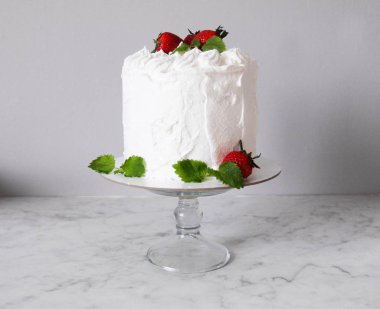 Krema ile büyük beyaz lezzetli pasta ve gri bir arka plan üzerinde şeffaf bir stand üzerinde çilek ve nane ile dekore  