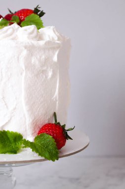 Krema ile büyük beyaz lezzetli pasta ve gri bir arka plan üzerinde şeffaf bir stand üzerinde çilek ve nane ile dekore  