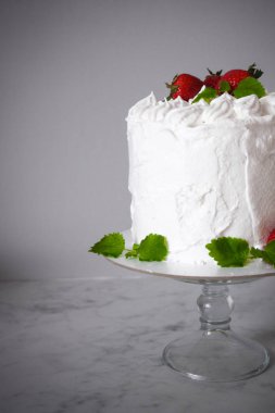 Krema ile büyük beyaz lezzetli pasta ve gri bir arka plan üzerinde şeffaf bir stand üzerinde çilek ve nane ile dekore  