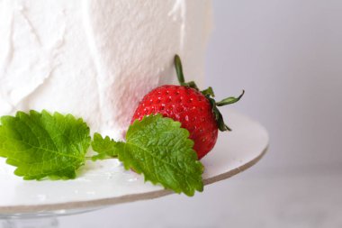 Krema ile büyük beyaz lezzetli pasta ve gri bir arka plan üzerinde şeffaf bir stand üzerinde çilek ve nane ile dekore  