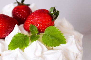 Krema ile büyük beyaz lezzetli pasta ve gri bir arka plan üzerinde şeffaf bir stand üzerinde çilek ve nane ile dekore  