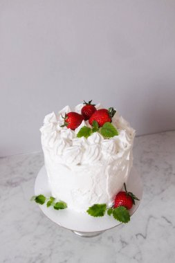 Krema ile büyük beyaz lezzetli pasta ve gri bir arka plan üzerinde şeffaf bir stand üzerinde çilek ve nane ile dekore  