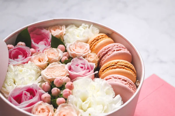 Gift round box with flowers, roses and macaroons almond cake with pink envelope on the table