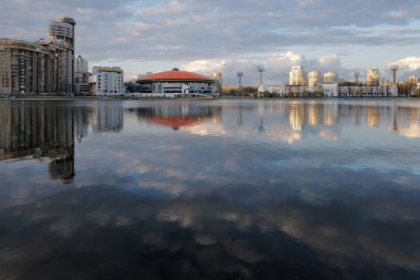 Şehir gün batımında bir gölete yansıyor.
